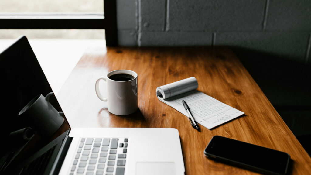 laptop computer sitting on desk with notepad and coffee mug.